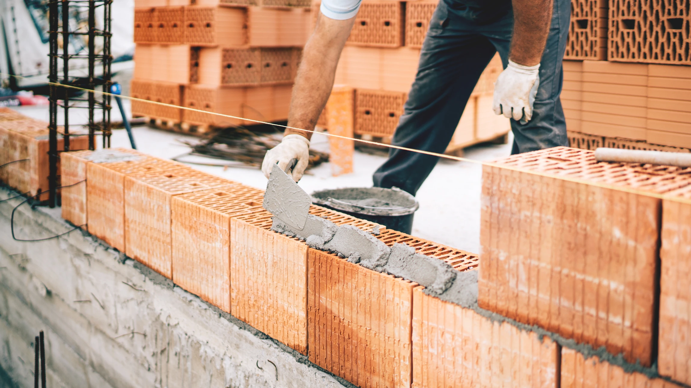 Ma&ccedil;on en salopette applique du mortier sur un mur de briques en terre cuite perfor&eacute;es sur chantier ext&eacute;rieur