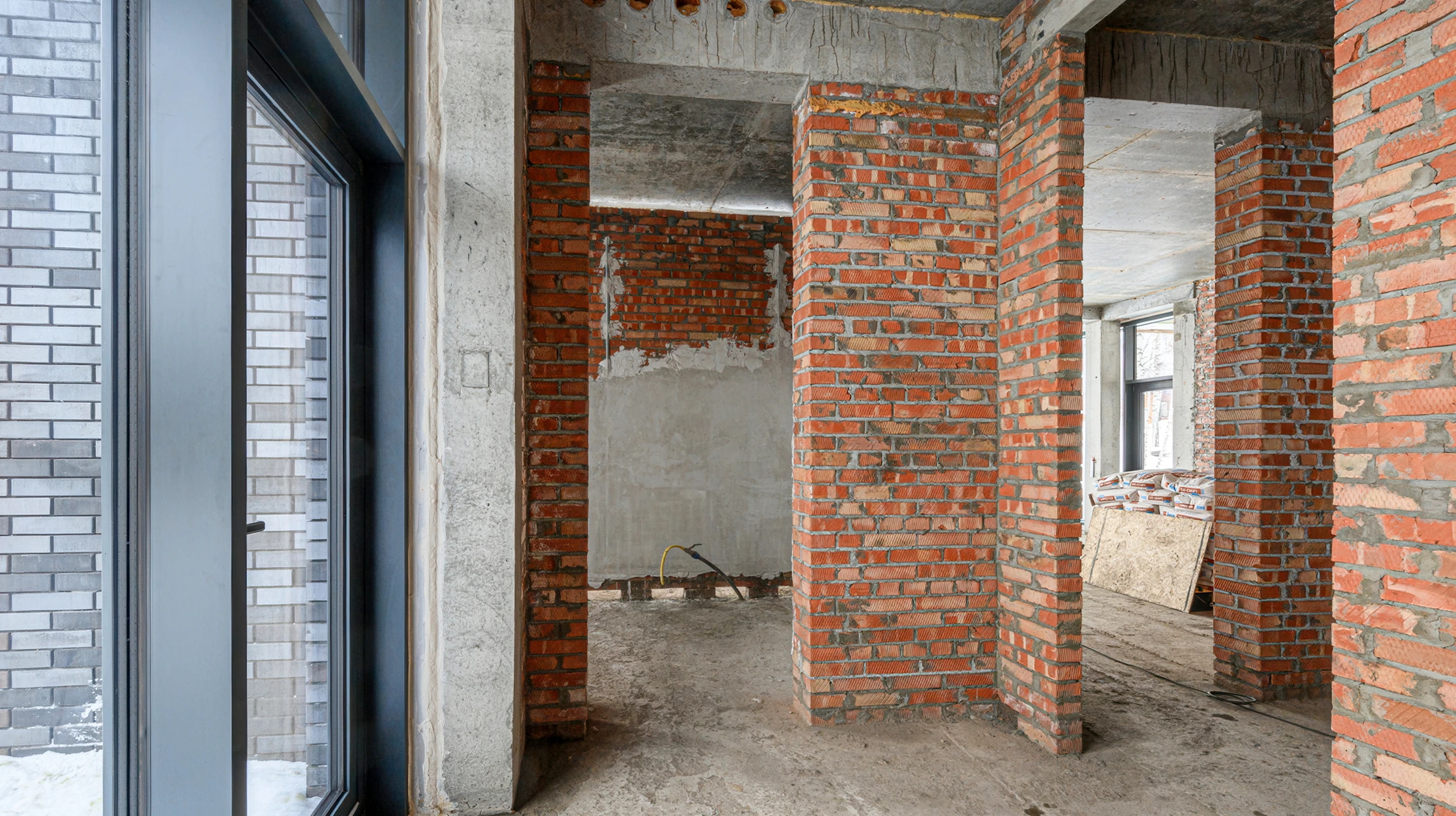 Chantier de construction intérieur avec ouvrier souriant en casque de sécurité blanc et combinaison bleue, portant gants orange, appuyé sur surface