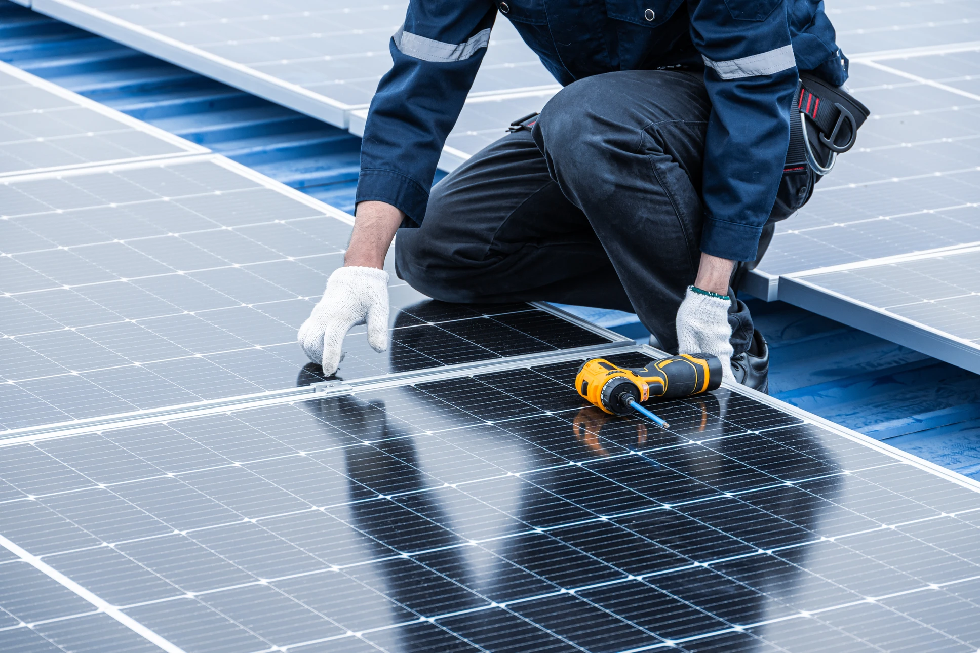 Ouvrier en combinaison blanche et casque de protection travaillant sur échafaudage extérieur, manipulant un élément de construction au niveau d'un bâtiment en béton avec fenêtres bleues