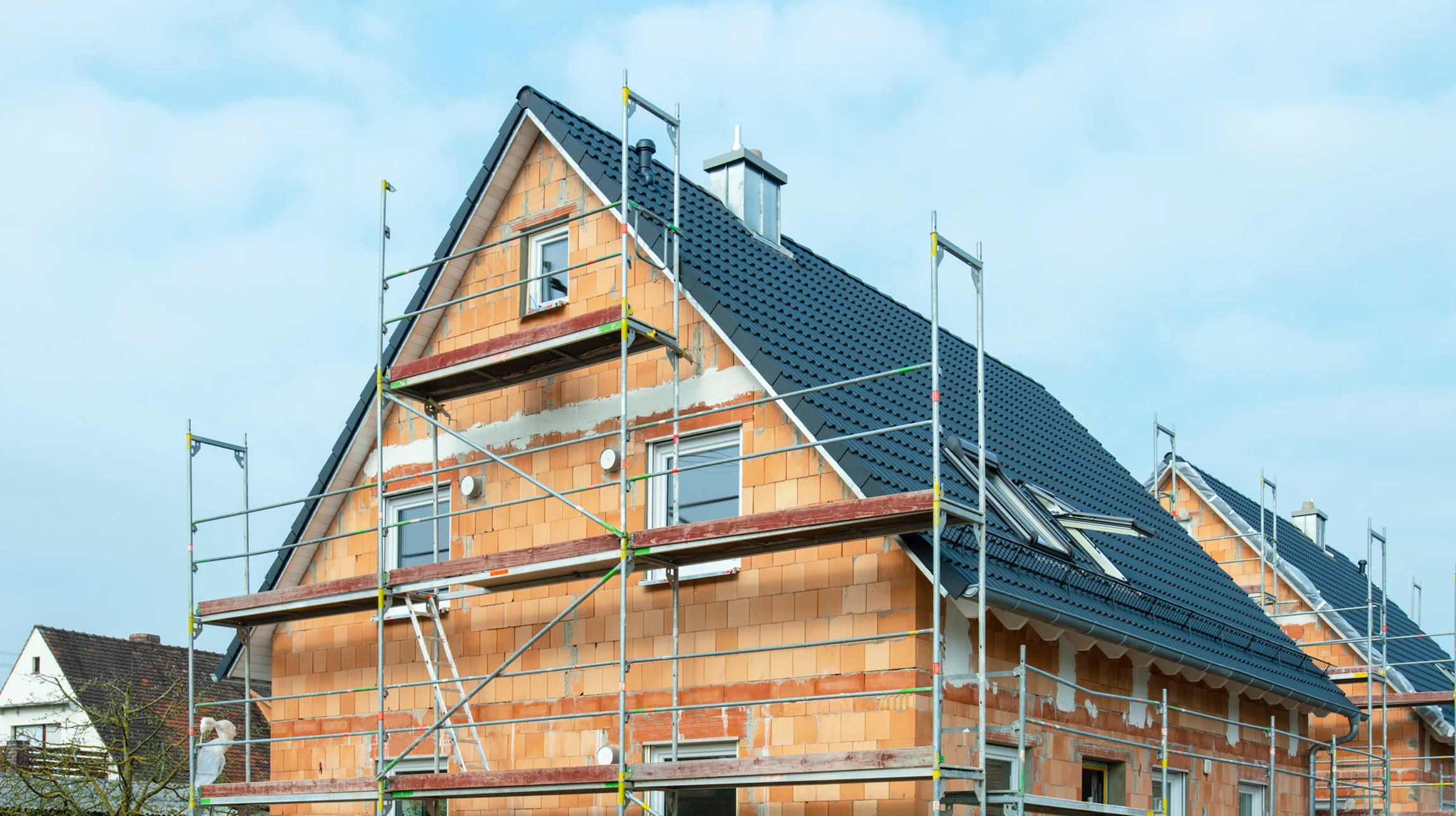 Chantier de construction extérieur avec homme en tenue de travail, casque de sécurité jaune, bras croisés devant bâtiments en construction