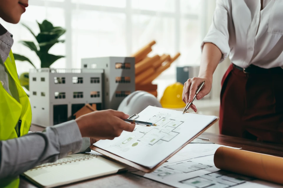 Ouvrier en vêtements de travail bleus et gants de protection jaunes utilisant un marteau à manche vert pour assembler une structure en bois